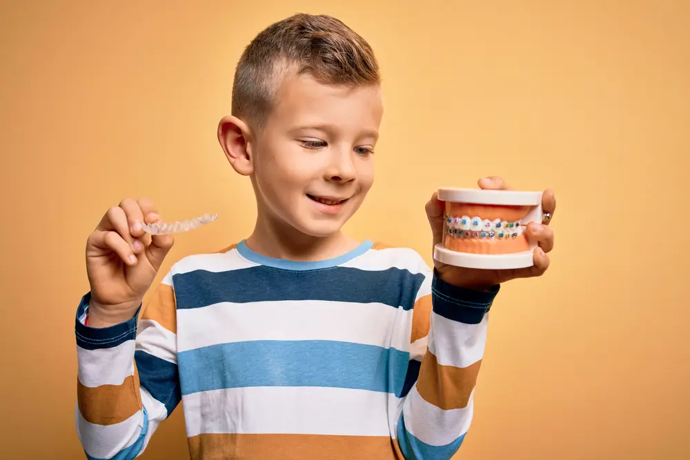 young boy holding metal braces typodont and clear aligners